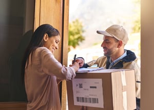 A smiling woman signs for a package delivery at her front door